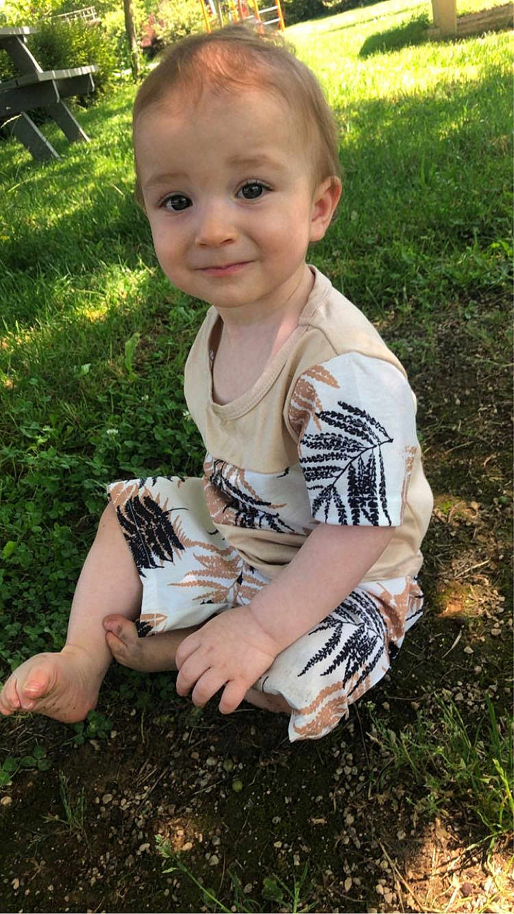 Fabien participe au concours pour gagner de l'argent avec cette photo : toddler, child, baby, grass, outdoors, sitting, bare_foot, smile, face, cheeks, hand, patterned_clothing, leaf_pattern, playground, picnic_table, sunlight, nature, dirt, portrait, curious