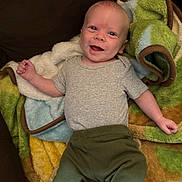 Liam joined the competition — help win amazing prizes! baby, smiling, infant, blanket, green_pants, gray_shirt, happy, lying_down, cute, face, child, young, cozy, soft_texture, indoors, person, close_up, portrait, bright_eyes, joyful