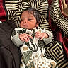 baby, newborn, infant, blanket, patterned_clothing, leaf_pattern, geometric_pattern, fabric, hand, face, sleepwear, cozy, soft_lighting, portrait, person, cute, small, resting, indoors, child