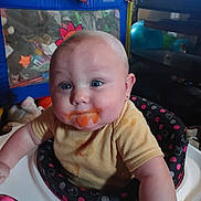 Sarah joined the competition — help win amazing prizes! baby, baby_food, black, blue_eyes, child, curious_expression, cute, face, feeding_time, high_chair, home, indoor, infant, messy_face, person, pink, playpen, sitting, toys, yellow_shirt