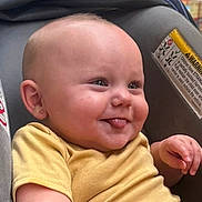 Sarah is registered to the contest to win money with this photo: baby, child, tongue_out, yellow_shirt, car_seat, smiling, face, earring, skin, infant, cute, playful, comfort, seat, fabric, warning_label, closeup, head, expression, happy