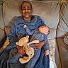 elderly_person, baby, blanket, plush_toy, couch, living_room, cozy, clothing, person, indoor, family, comfort, smile, holding, seated, relaxation, home, infant, soft_lighting, tender_moment