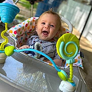Hayes is registered to the contest to win money with this photo: baby, child, walker, toy, smile, happy, indoor, colorful, face, polka_dot, cushion, clothing, blonde_hair, expression, person, seat, playful, background, blurred, joyful