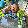 baby, child, walker, toy, smile, happy, indoor, colorful, face, polka_dot, cushion, clothing, blonde_hair, expression, person, seat, playful, background, blurred, joyful