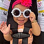 baby, child, sunglasses, headband, pink_flower, car_seat, smile, happy, waving_hand, bracelet, black_straps, orange_shirt, infant, cute, accessory, portrait, seatbelt, safety, closeup, fashion