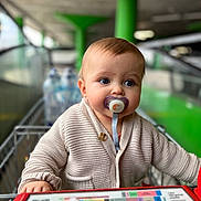 Luis a rejoint le concours — aidez-le/la à gagner de superbes lots ! baby, child, pacifier, shopping_cart, sweater, blue_eyes, indoor, person, cute, infant, portrait, hand, blurred_background, retail, store, shopping, seat, clothing, young_child, face