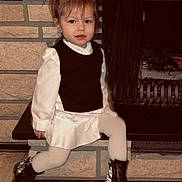 Inaya participe au concours pour gagner de l'argent avec cette photo : bench, black_vest, boots, brick_wall, child, clothing, cozy, dress, face, fireplace, floor_tiles, girl, hearth, indoor, pigtails, portrait, sitting, smiling, toddler, white_tights