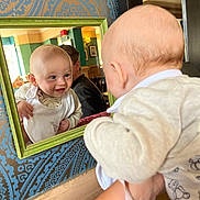 Luca joined the competition — help win amazing prizes! baby, mirror, reflection, smile, indoor, face, infant, clothing, bib, hand, person, wallpaper, pattern, frame, adult, furniture, light, curiosity, portrait, holding