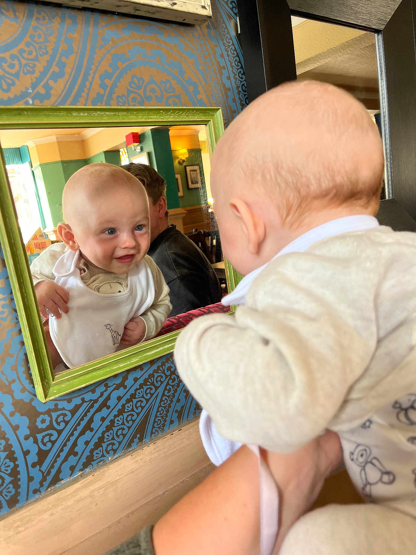 Luca joined the competition — help win amazing prizes! baby, mirror, reflection, smile, indoor, face, infant, clothing, bib, hand, person, wallpaper, pattern, frame, adult, furniture, light, curiosity, portrait, holding