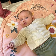 éléanor participe au concours pour gagner de l'argent avec cette photo : baby, infant, child, play_mat, floral_pattern, sweater, pants, hand, foot, person, indoor, soft_lighting, blanket, cute, pale_skin, expression, lying_down, tiny_fist, casual_clothing, relaxed