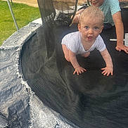 Elio participe au concours pour gagner de l'argent avec cette photo : child, baby, toddler, trampoline, netting, outdoor, grass, brick_wall, crawling, glasses, smiling, play, safety_net, padding, person, fun, summer, happy, curious, backyard