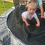 child, baby, toddler, trampoline, netting, outdoor, grass, brick_wall, crawling, glasses, smiling, play, safety_net, padding, person, fun, summer, happy, curious, backyard