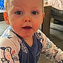 Elio participe au concours pour gagner de l'argent avec cette photo : toddler, child, indoor, face, blue_eyes, blonde_hair, shirt, patterned_clothing, living_room, furniture, couch, table, toy, floor, curious, person, closeup, expression, young_child, home