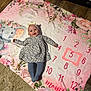 baby, infant, child, blanket, floral, milestone_blanket, numbers, headband, bow, dress, tights, smile, lying_down, floor, wooden_floor, rug, elephant_illustration, portrait, framed_photo, cozy