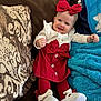 baby, infant, headband, bow, red_dress, white_shoes, red_tights, smile, face, couch, patterned_pillow, turquoise_blanket, button, cozy, portrait, sitting, adorable, child_clothing, plush_texture, home_interior
