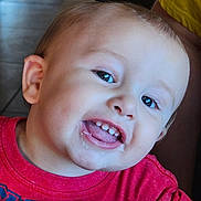Jedi is registered to the contest to win money with this photo: toddler, child, smiling, happy, face, mouth, teeth, tongue, red_shirt, hand, wooden_table, indoor, skin, hair, eyes, closeup, person, cute, expression, baby