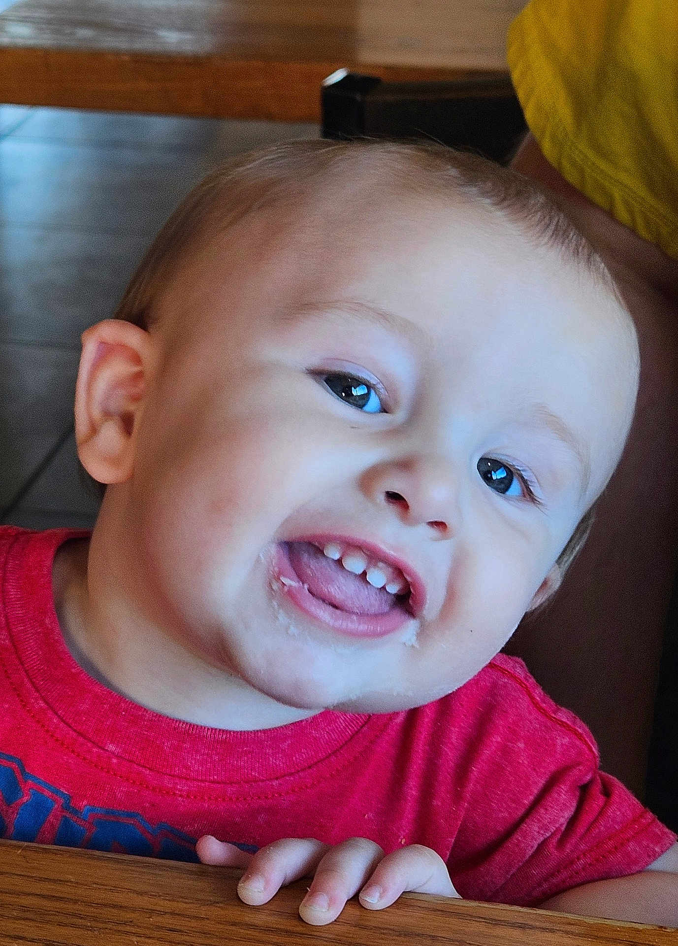 Jedi is registered to the contest to win money with this photo: toddler, child, smiling, happy, face, mouth, teeth, tongue, red_shirt, hand, wooden_table, indoor, skin, hair, eyes, closeup, person, cute, expression, baby