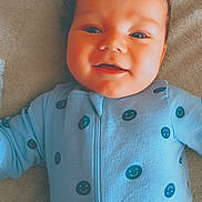 Kane is registered to the contest to win money with this photo: baby, blanket, blue_onesie, child, clothing, comfort, cute, expression, face, happy, head, indoors, infant, lying_down, portrait, skin, smile, smiley_face, soft_texture, young