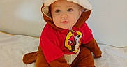 Dean is registered to the contest to win money with this photo: animal_costume, baby, brown_clothing, child, costume, curious, cute, expression, face, floor, headwear, indoor, infant, portrait, red_clothing, single_person, sitting, soft_surface, wall, young_child