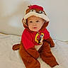 Dean is registered to the contest to win money with this photo: baby, child, costume, animal_costume, red_clothing, brown_clothing, sitting, indoor, soft_surface, cute, portrait, face, headwear, infant, young_child, expression, curious, single_person, wall, floor