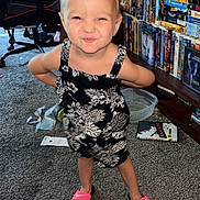 Raya joined the competition — help win amazing prizes! child, toddler, smiling_child, standing, floral_dress, pink_slides, carpeted_floor, bookshelf, vhs_tapes, dvd_cases, living_room, gaming_chair, computer_monitor, desk, plastic_bowl, playful_pose, candid_photo, blond_hair, clutter, home_interior