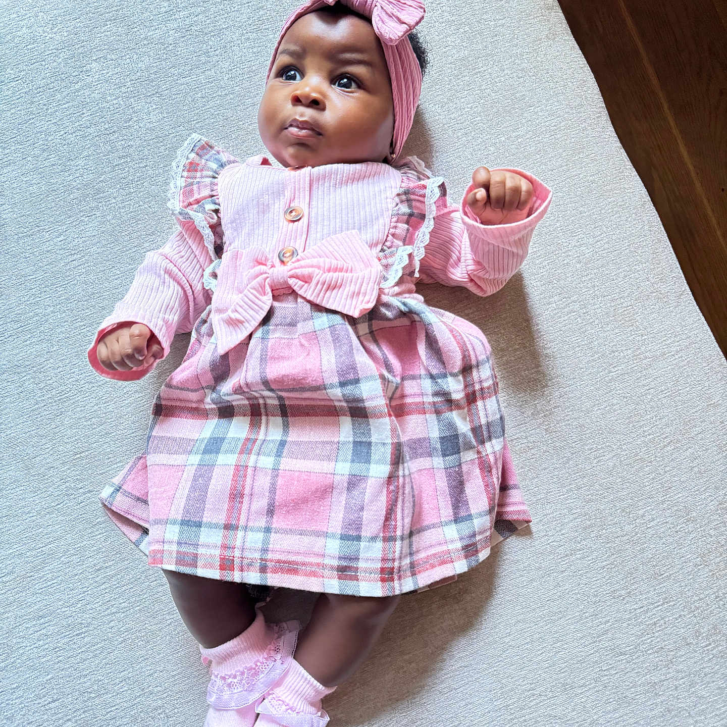 Laurel is registered to the contest to win money with this photo: adorable, baby, child, clothing, cute, feet, female, floor, hands, headband, indoors, infant, light_texture, looking_up, lying_down, pink_dress, plaid_pattern, portrait, socks, wood_floor