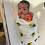 Cleo is registered to the contest to win money with this photo: baby, infant, blanket, bee_pattern, mattress, crib, orange_clothing, striped, strawberry, wrapped, newborn, child, indoors, cute, portrait, bed, soft, sleeping_area, person, warm