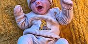 Aleksandra is registered to the contest to win money with this photo: apparel, baby, blanket, child, cozy, cute, face, feet, happy, hat, infant, knitwear, lying_down, mittens, pattern, portrait, smiling, soft_texture, warm_clothing, yellow