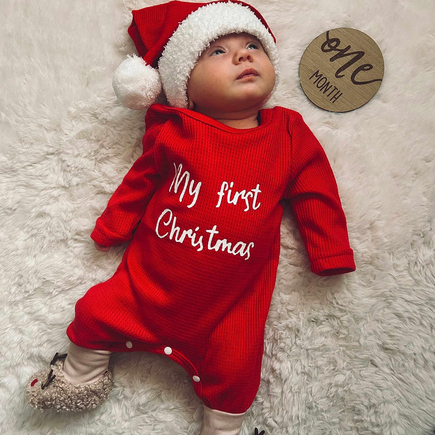 Aleksandra is registered to the contest to win money with this photo: baby, celebration, child, christmas, cozy, cute, festive, fluffy_rug, holiday, indoors, infant, lying_down, one_month, portrait, red_onesie, reindeer_slippers, santa_hat, soft, warm, wooden_sign