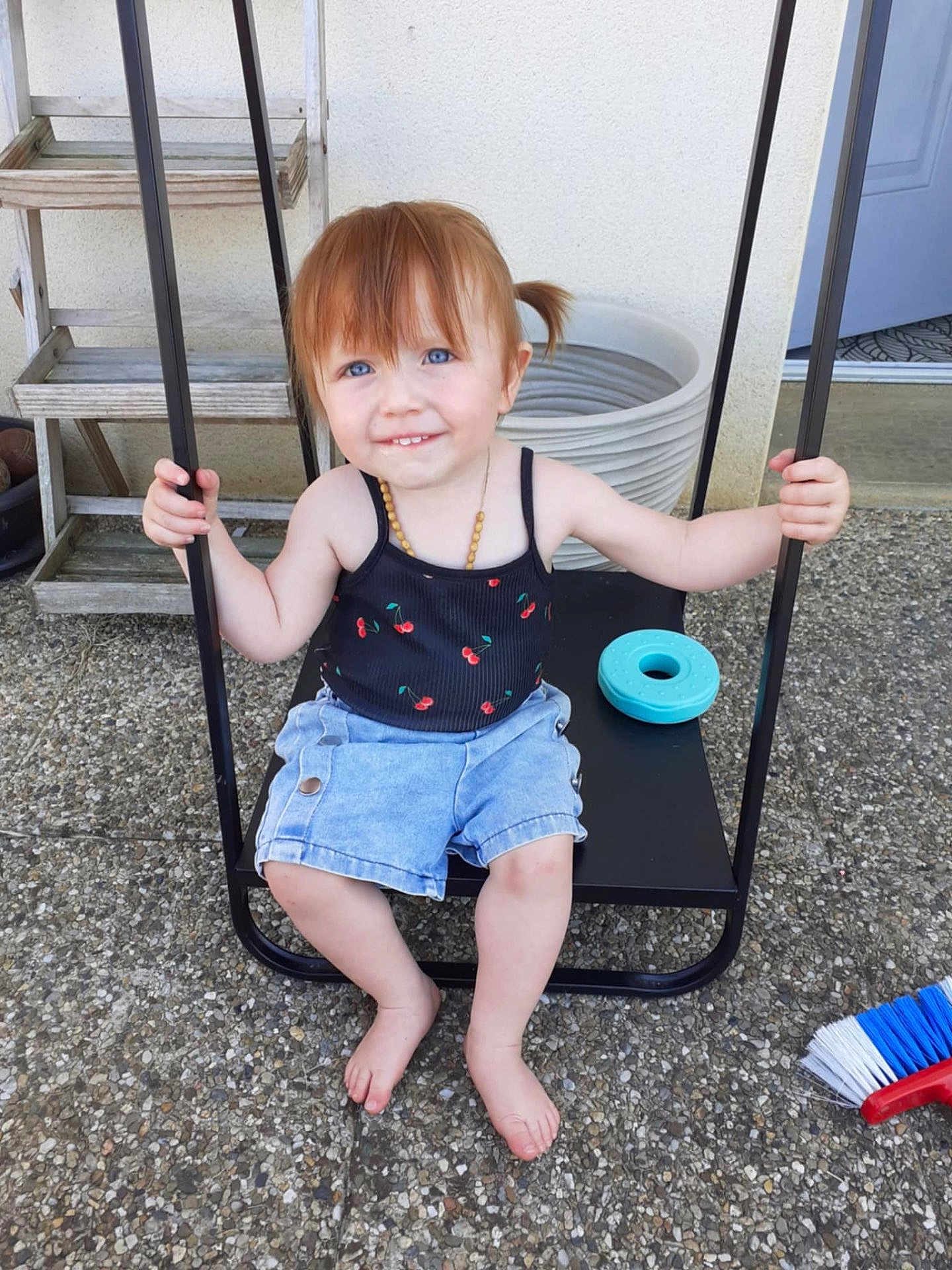Meloane participe au concours pour gagner de l'argent avec cette photo : barefoot, black_swing, blue_eyes, broom, casual_clothing, child, denim_shorts, holding, outdoor, patio, pebble_stone, person, pigtails, playful, smiling, summer, swing, tank_top, toddler, toy
