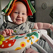 Zaylee is registered to the contest to win money with this photo: baby, smiling, indoor, toy, colorful, fabric_book, child, happy, playful, patterned, clothing, seat, hand, arm, face, infant, furniture, cute, expression, closeup