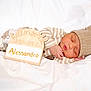 baby, newborn, sleeping, hat, striped_clothing, wooden_sign, name_plate, blanket, white_bedding, cozy, peaceful, portrait, infant, closed_eyes, hand, soft_texture, newborn_photo, prop, studio_lighting, cute