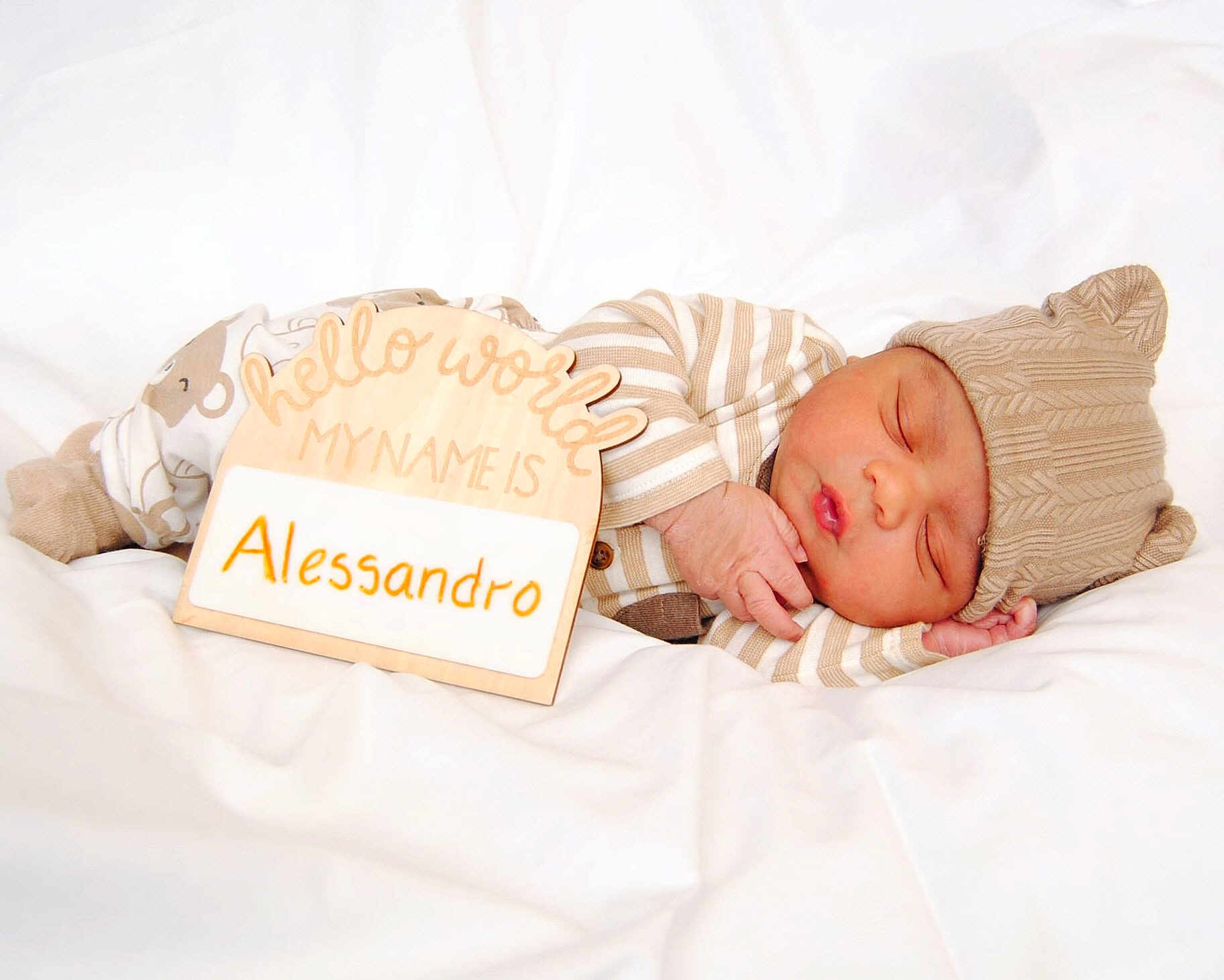 Alessandro joined the competition — help win amazing prizes! baby, newborn, sleeping, hat, striped_clothing, wooden_sign, name_plate, blanket, white_bedding, cozy, peaceful, portrait, infant, closed_eyes, hand, soft_texture, newborn_photo, prop, studio_lighting, cute