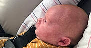 Joseph is registered to the contest to win money with this photo: baby, infant, car_seat, child, safety_harness, pacifier, striped_clothing, mustard_color, seat_belt, warning_label, no_smoking_sign, side_profile, head, face, ears, newborn, indoor, fabric, blanket, closeup