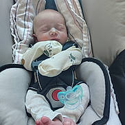 Joseph is registered to the contest to win money with this photo: baby, infant, sleeping, car_seat, pacifier, clothing, blanket, foot, footwear, child, person, resting, comfort, cute, newborn, fabric, seatbelt, soft, indoors, peaceful