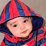baby, child, hoodie, striped_clothing, red, blue, couch, indoor, face, eyes, hand, cute, infant, portrait, young, expression, casual, sitting, cozy, soft_furniture