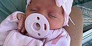 Rylee is registered to the contest to win money with this photo: baby, newborn, sleeping, pacifier, pink_clothing, headband, bow, arm, hand, outdoor, balcony, railing, person, infant, cute, soft_fabric, resting, peaceful, closeup, portrait