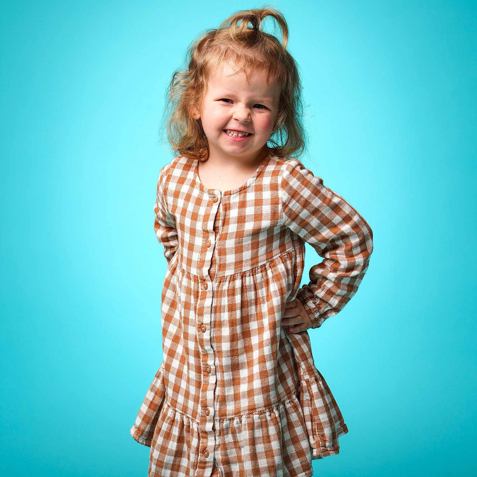 Leaghan joined the competition — help win amazing prizes! blue_background, buttoned_dress, casual_clothing, checkered_pattern, child, confident, curly_hair, dress, fashion, girl, happy, long_sleeves, playful, portrait, posing, smile, standing, studio, topknot, young