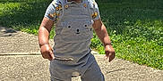 Aziah joined the competition — help win amazing prizes! toddler, child, pacifier, stick, sidewalk, grass, trees, sunlight, shadow, outdoor, curly_hair, grey_overalls, short_sleeve_shirt, socks, building, van, daytime, person, playful, walking