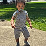 toddler, child, pacifier, stick, sidewalk, grass, trees, sunlight, shadow, outdoor, curly_hair, grey_overalls, short_sleeve_shirt, socks, building, van, daytime, person, playful, walking