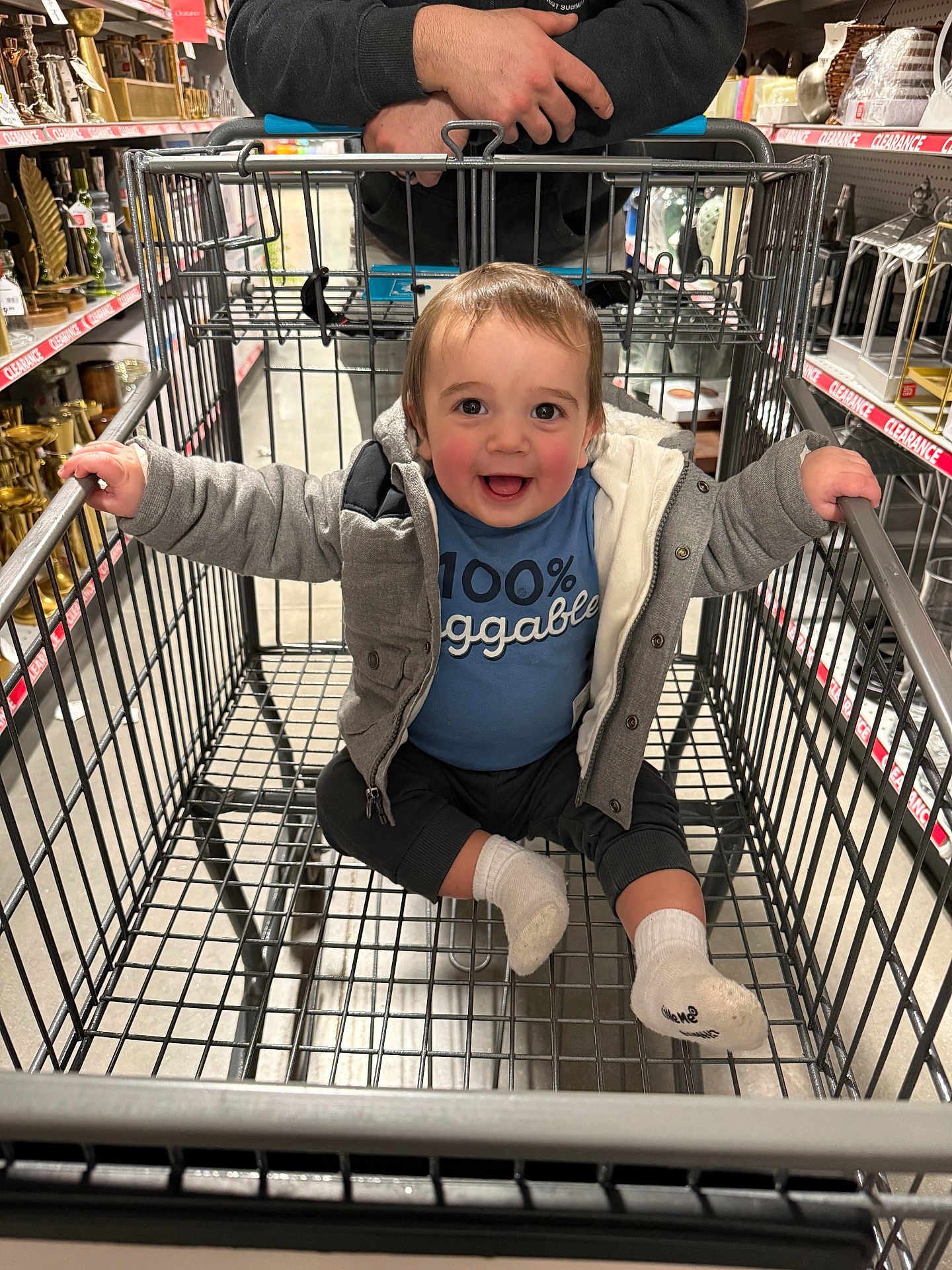 Alexander is registered to the contest to win money with this photo: child, toddler, baby, shopping_cart, supermarket, store_aisle, smile, happy, jacket, socks, clothing, person, sitting, metal_grid, parent_hands, retail, clearance_sign, shelves, portrait, candid