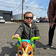 Alexander joined the competition — help win amazing prizes! adult, asphalt, car, child, cute, daylight, fun, jacket, outdoor, parking_lot, person, play, shoes, smile, sunglasses, toddler, tongue_out, toy, toy_horse, vehicle