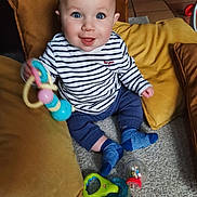 Elio participe au concours pour gagner de l'argent avec cette photo : baby, child, toy, blue_eyes, striped_shirt, socks, pillow, carpet, smiling, indoor, cute, seated, playful, colorful_toy, happy, infant, home, floor, person, portrait