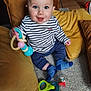 baby, child, toy, blue_eyes, striped_shirt, socks, pillow, carpet, smiling, indoor, cute, seated, playful, colorful_toy, happy, infant, home, floor, person, portrait