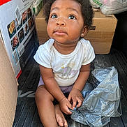Elyse is registered to the contest to win money with this photo: toddler, child, sitting, curious, plastic_bag, cardboard_box, floor, clothing, shorts, indoor, baby, person, cute, expression, earring, black_hair, casual, looking_up, small_hands, barefoot