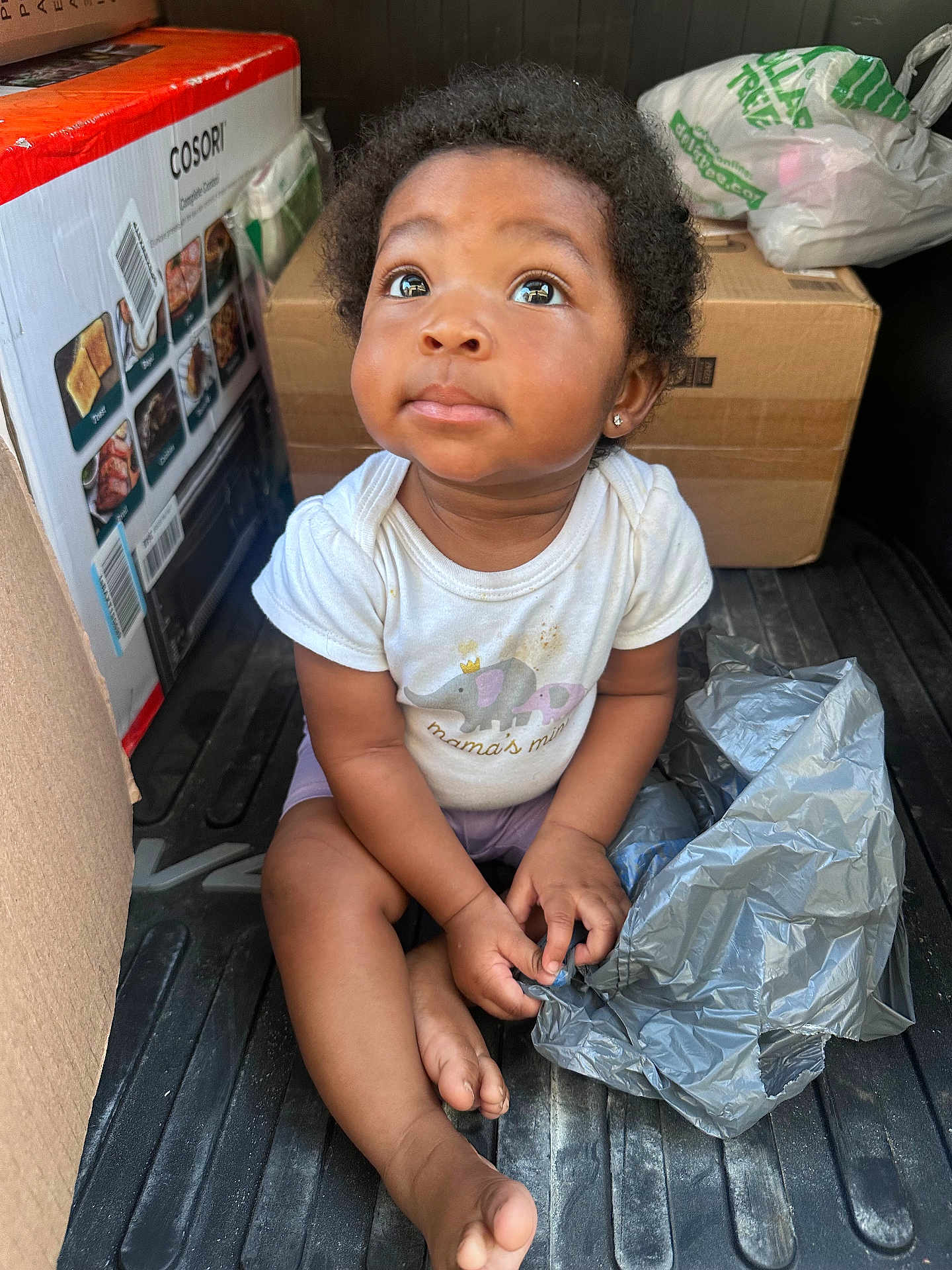 Elyse is registered to the contest to win money with this photo: toddler, child, sitting, curious, plastic_bag, cardboard_box, floor, clothing, shorts, indoor, baby, person, cute, expression, earring, black_hair, casual, looking_up, small_hands, barefoot