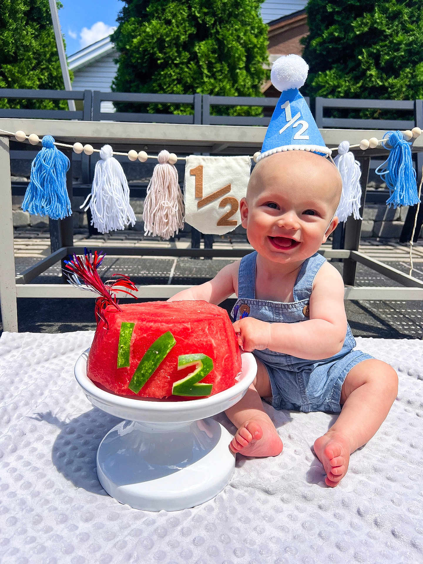 Brooks joined the competition — help win amazing prizes! baby, smiling, party_hat, watermelon, cake, outdoor, blanket, denim_overalls, celebration, half_birthday, tassel_garland, banner, sunlight, grass, foot, hands, face, happy, summer, table