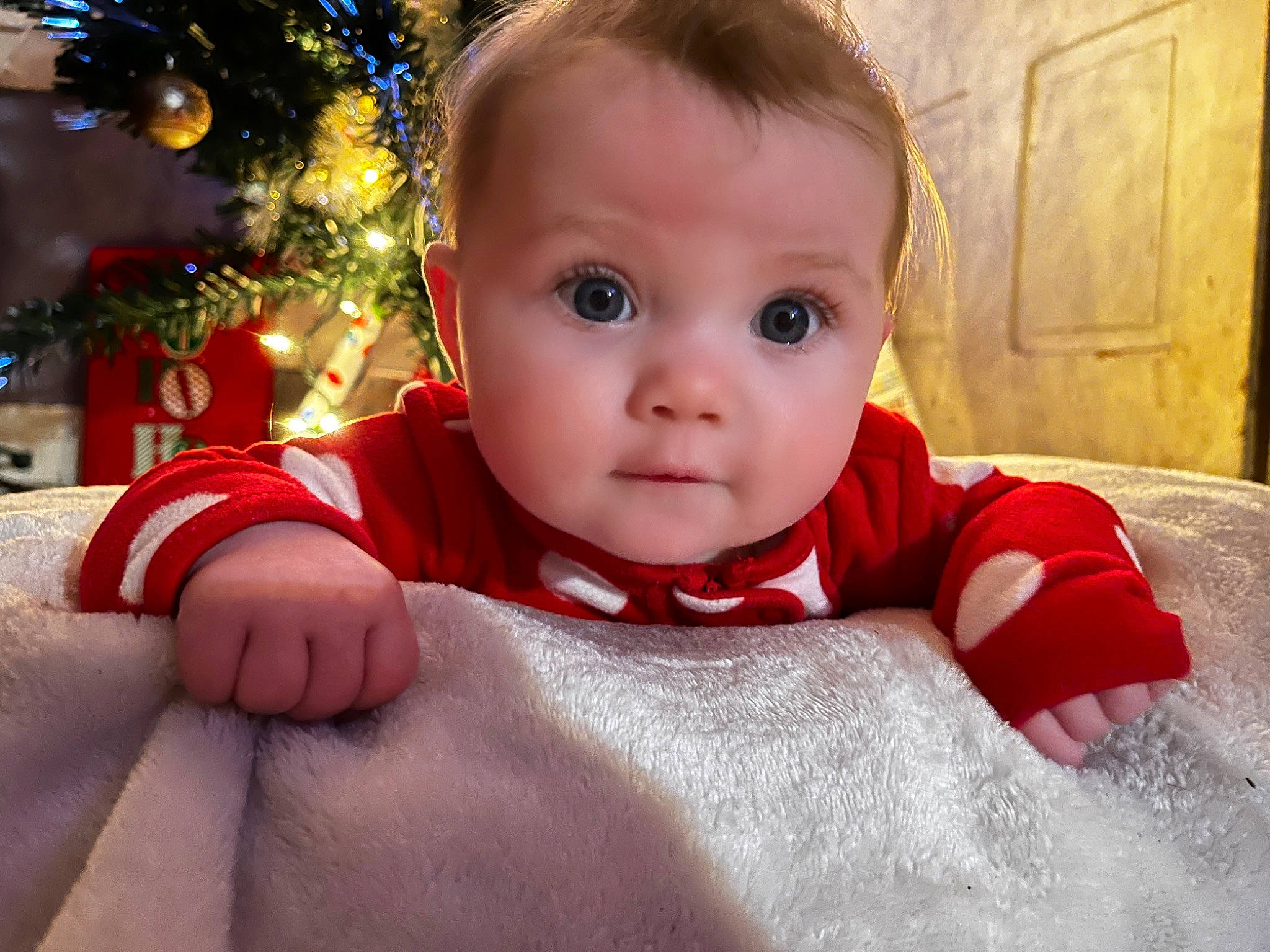 Tessa joined the competition — help win amazing prizes! baby, baby_toddler_clothing, cheek, child, christmas_tree, comfort, event, facial_expression, flooring, fun, happy, holiday, linens, ornament, person, sitting, skin, sleeve, standing, toddler