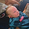 baby, child, infant, portrait, face, eyes, looking_up, blond_hair, smiling, blue_clothing, hoodie, levis, bottle, living_room, couch, coffee_table, backpack, tattoo, adult_arm, indoor