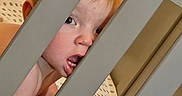 Bennett is registered to the contest to win money with this photo: baby, bars, bed, bedding, child, crib, cute, expression, face, head, indoors, infant, peek, person, playful, polka_dot, red_hair, skin, tongue_out, young_child